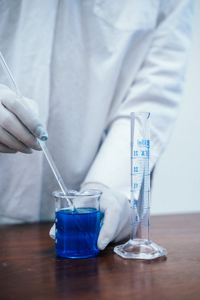 Close-up of a scientist mixing blue liquid in a beaker for a chemistry experiment.